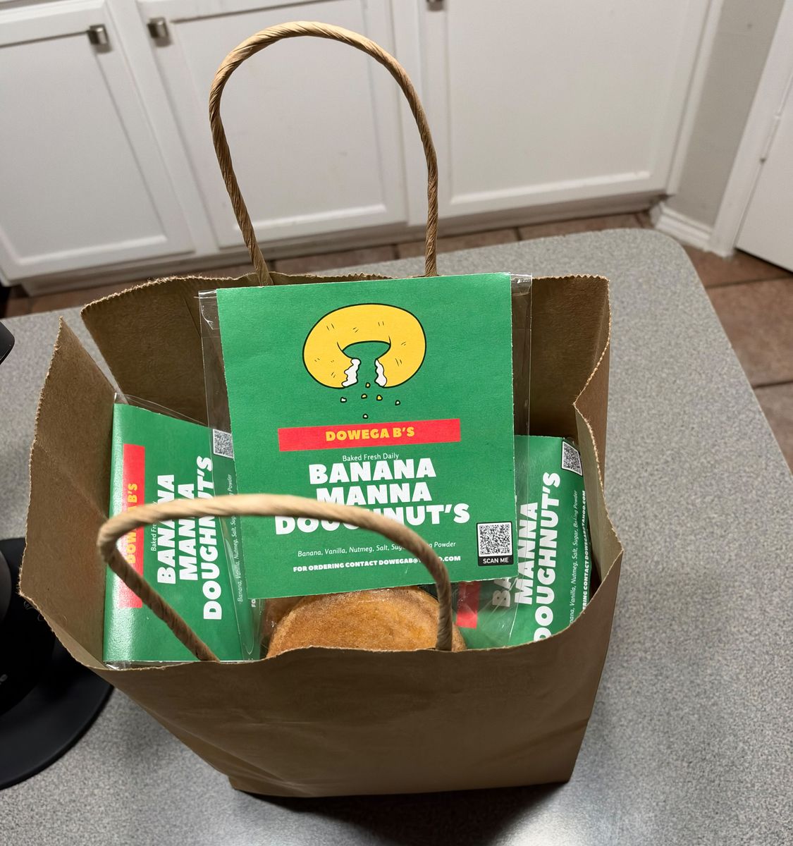 A brown kraft bag packed with labeled banana manna doughnuts